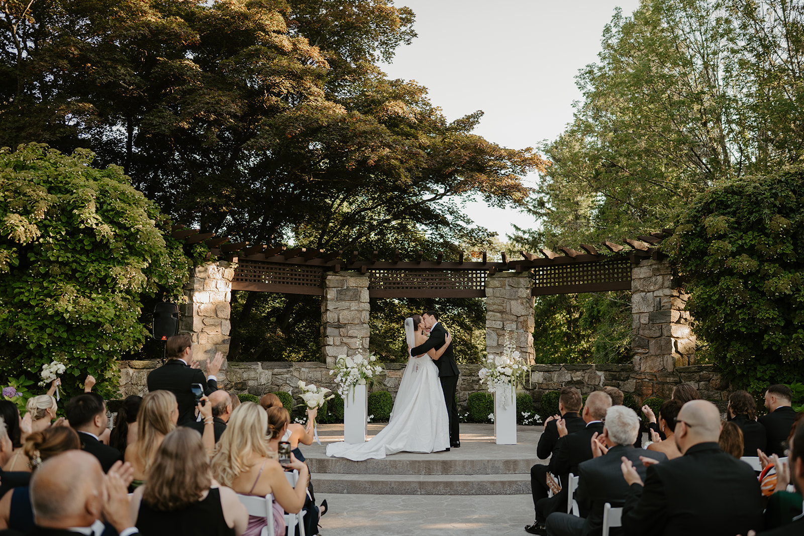 Bride and groom share their first kiss at the stone altar while seated guests applaud in celebration.